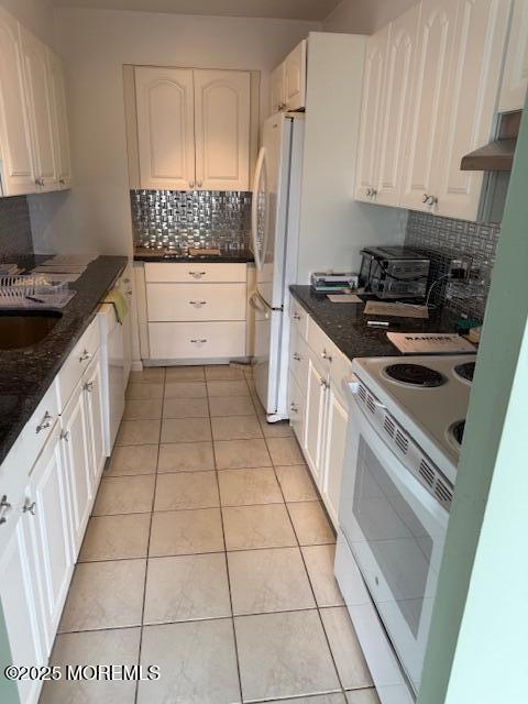 kitchen featuring electric stove, backsplash, white cabinetry, freestanding refrigerator, and light tile patterned floors