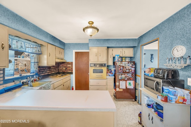 kitchen with under cabinet range hood, light countertops, cream cabinetry, white appliances, and a sink