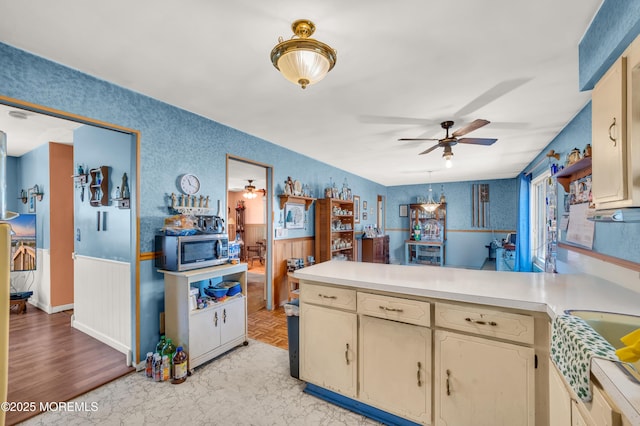 kitchen with a ceiling fan, a peninsula, light countertops, wainscoting, and stainless steel microwave