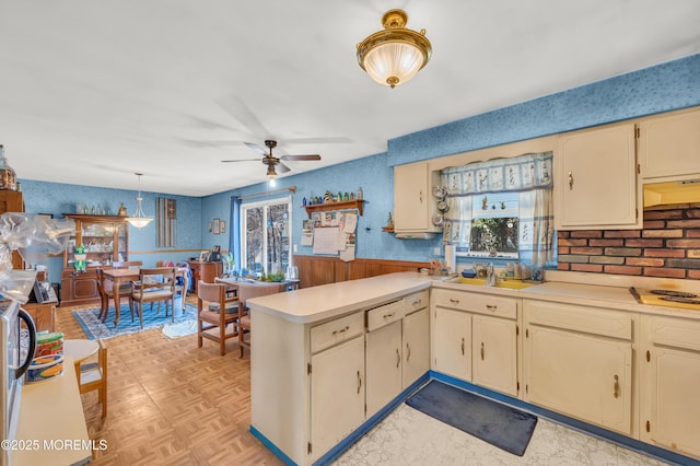 kitchen with a ceiling fan, a peninsula, light countertops, under cabinet range hood, and cream cabinets