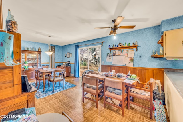 dining room with a wainscoted wall, wallpapered walls, and ceiling fan