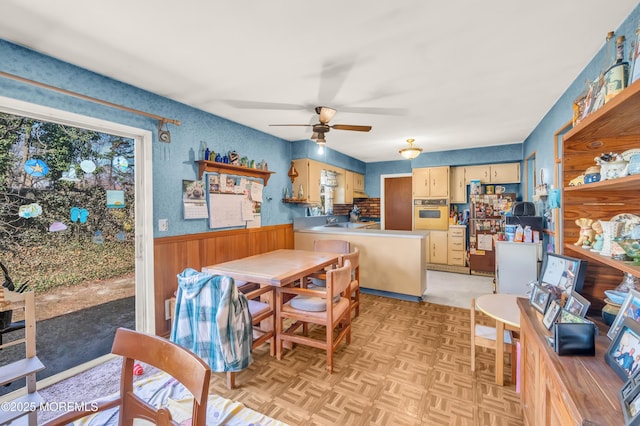 dining area with wooden walls, a ceiling fan, and wainscoting