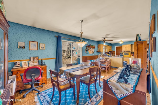 dining area featuring a wainscoted wall, a ceiling fan, and wallpapered walls