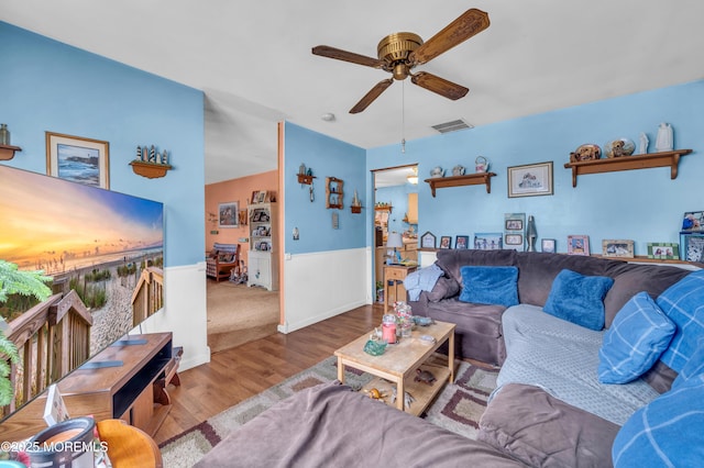 living area featuring visible vents, wood finished floors, ceiling fan, and wainscoting