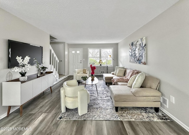 living room featuring baseboards, a textured ceiling, wood finished floors, and stairs