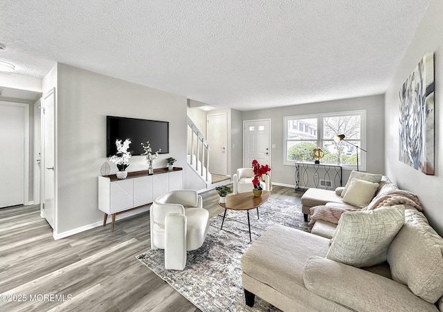 living room featuring stairway, a textured ceiling, baseboards, and wood finished floors