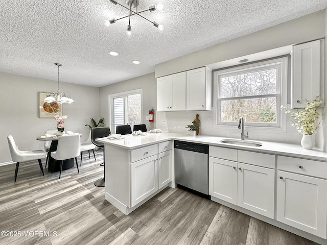 kitchen featuring a peninsula, a sink, light wood-style floors, dishwasher, and a notable chandelier