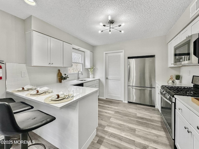 kitchen with light countertops, light wood-type flooring, appliances with stainless steel finishes, white cabinets, and a sink