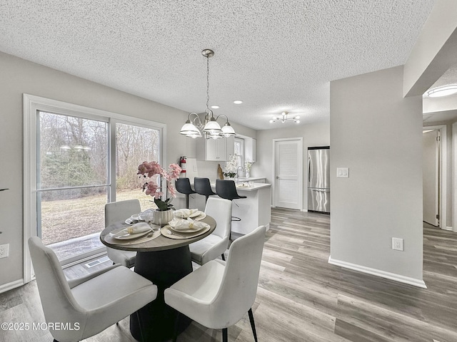 dining area with light wood-type flooring, baseboards, a notable chandelier, and a textured ceiling