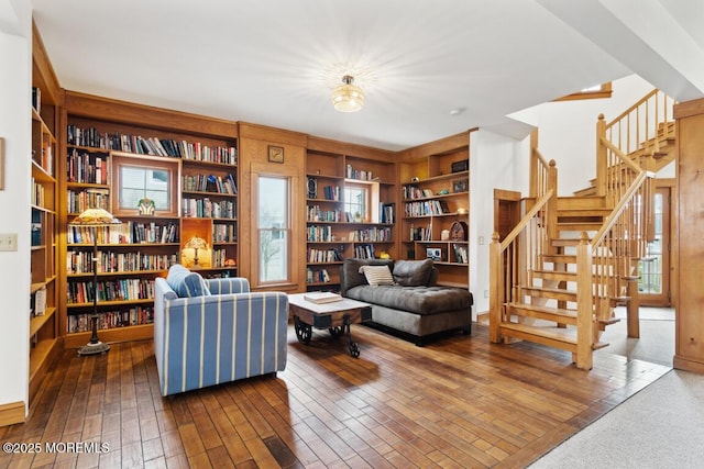 living area with stairs, bookshelves, and dark wood-style flooring