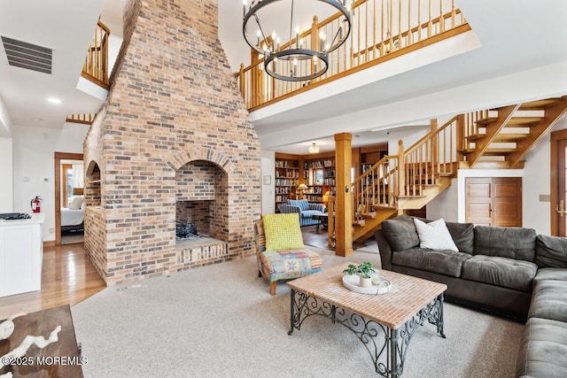 living room featuring visible vents, wood finished floors, stairway, a brick fireplace, and a chandelier