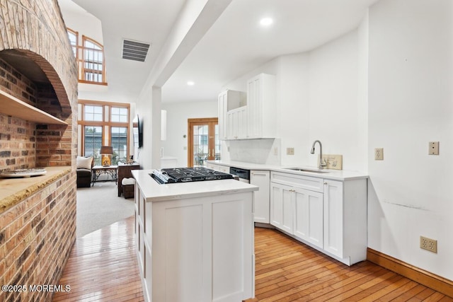 kitchen featuring visible vents, a center island, light wood-style floors, white cabinets, and a sink