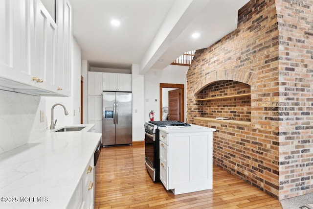 kitchen featuring light wood finished floors, brick wall, appliances with stainless steel finishes, white cabinetry, and a sink