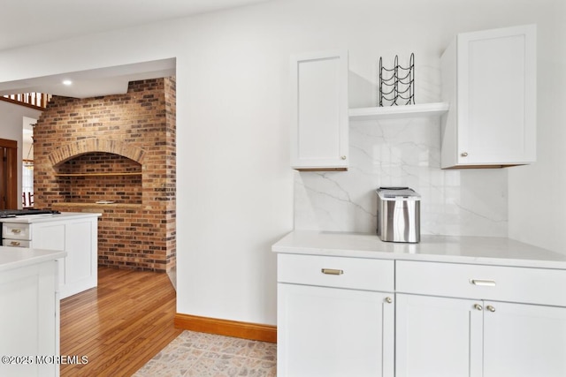 kitchen with light wood finished floors, open shelves, light countertops, white cabinetry, and backsplash