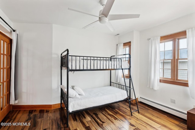 bedroom featuring a baseboard heating unit, wood-type flooring, baseboards, and a ceiling fan