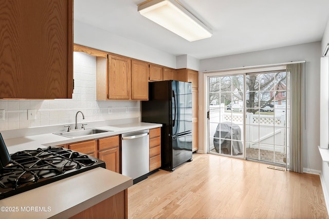 kitchen featuring black appliances, light wood-style flooring, light countertops, and a sink