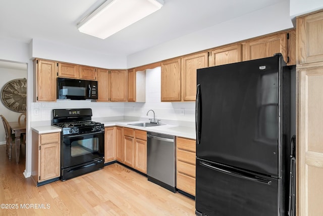 kitchen featuring a sink, black appliances, light countertops, light wood-style floors, and backsplash