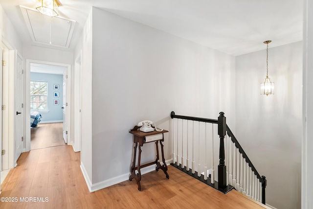 corridor with baseboards, an upstairs landing, attic access, and light wood finished floors