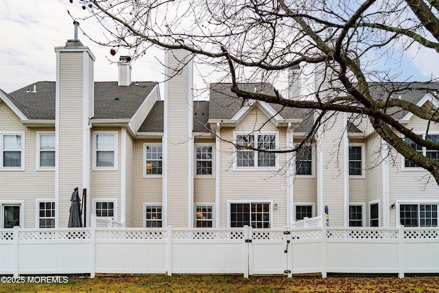 rear view of house featuring a fenced front yard and a chimney