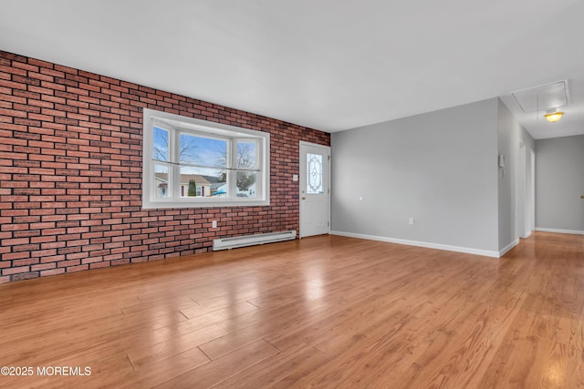 unfurnished living room featuring a baseboard heating unit, attic access, light wood-type flooring, and brick wall