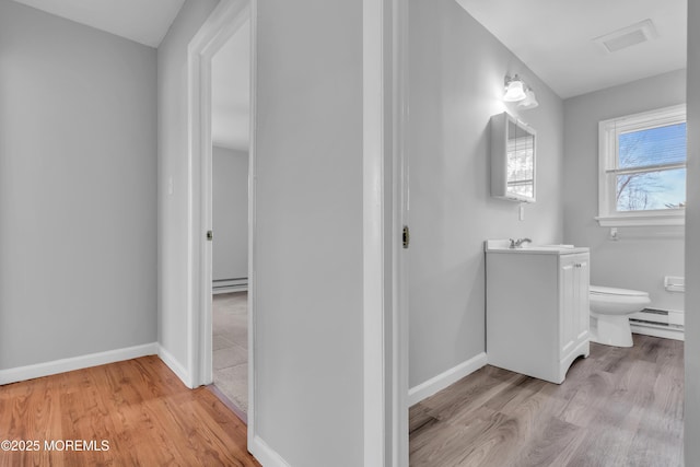 bathroom with toilet, a baseboard heating unit, wood finished floors, baseboards, and vanity