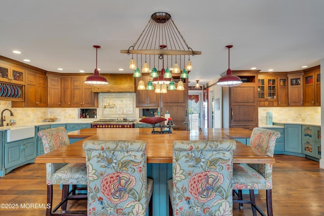 kitchen with tasteful backsplash, glass insert cabinets, pendant lighting, wood finished floors, and a sink