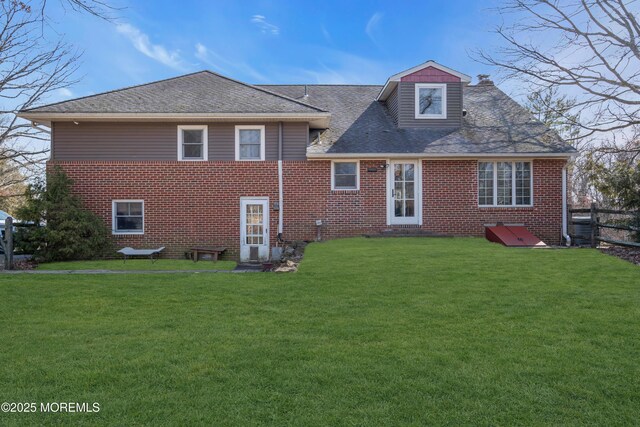 rear view of house featuring fence, a lawn, and brick siding