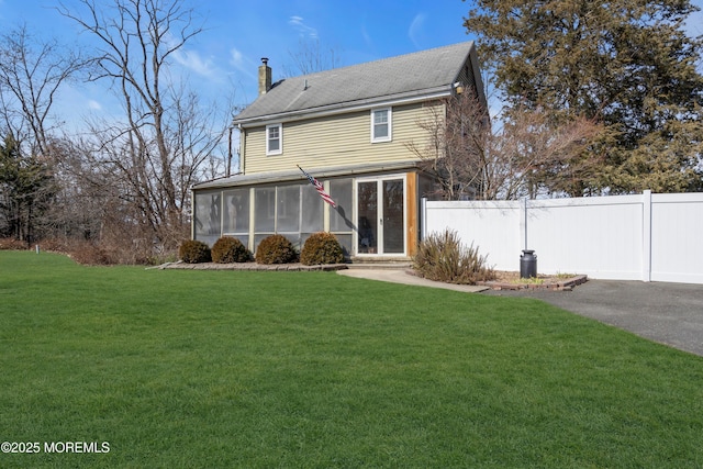 back of house featuring a lawn, a chimney, fence, and a sunroom