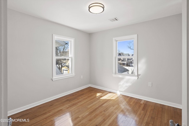 unfurnished room with visible vents, baseboards, and hardwood / wood-style floors