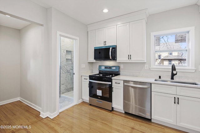 kitchen with light wood finished floors, a sink, white cabinetry, stainless steel appliances, and light countertops