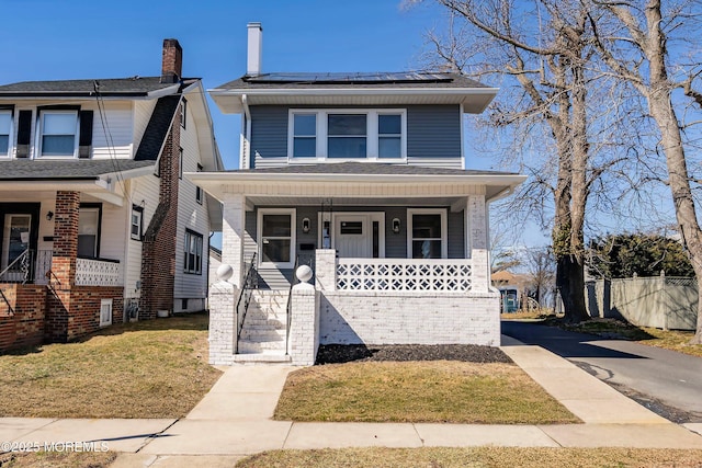 traditional style home featuring roof mounted solar panels, a porch, a front lawn, and fence