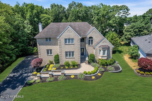 view of front of property featuring brick siding, a chimney, and a front lawn