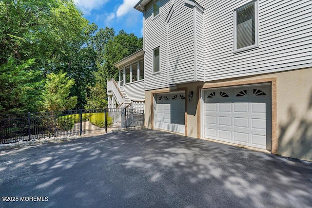 view of property exterior with an attached garage, fence, stairway, stucco siding, and driveway