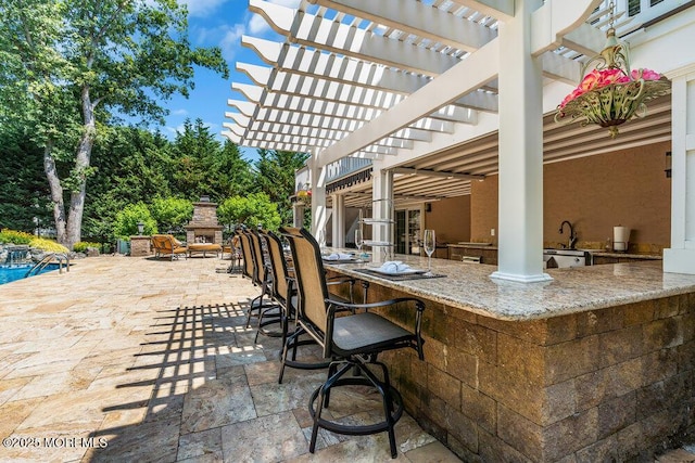 view of patio / terrace featuring an outdoor kitchen, outdoor dry bar, an outdoor stone fireplace, and a pergola