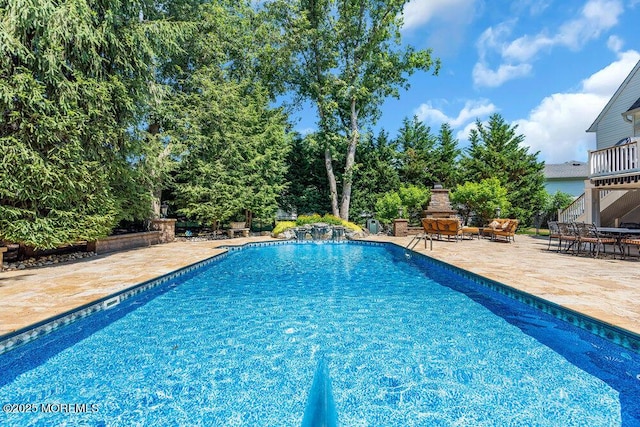 outdoor pool featuring an outdoor stone fireplace and a patio