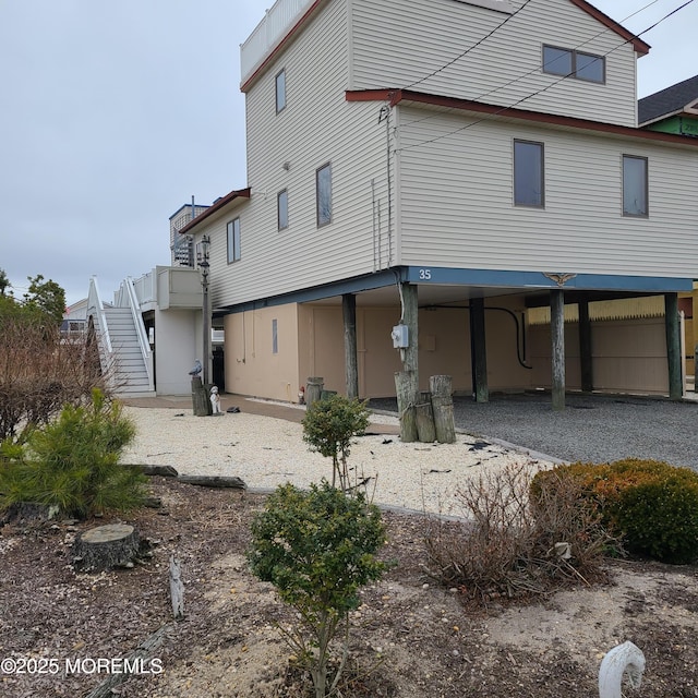 rear view of house featuring a carport, driveway, and stairs