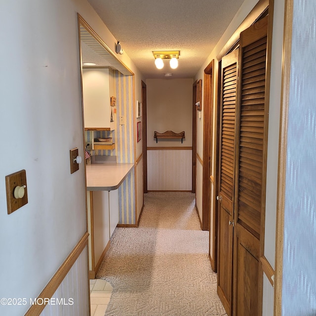 corridor featuring light carpet, a textured ceiling, and wainscoting