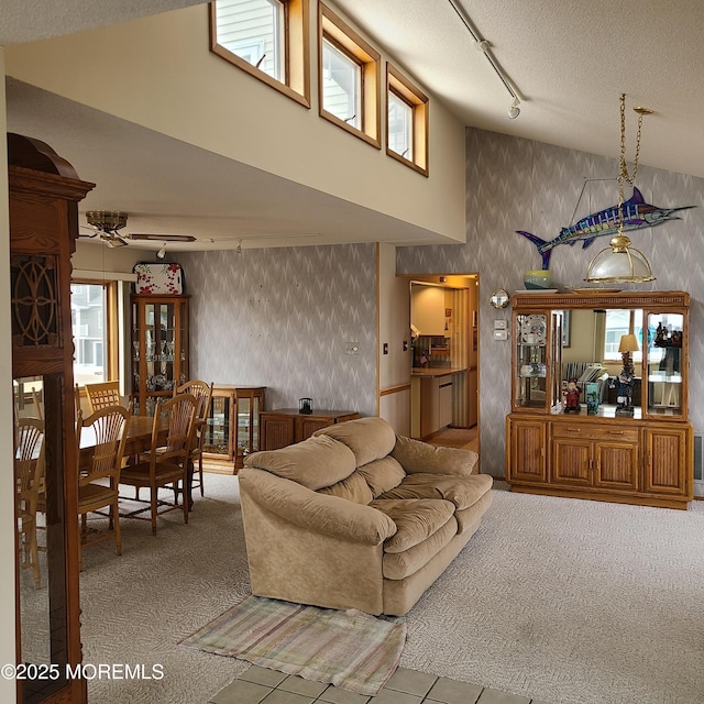 carpeted living room with high vaulted ceiling, wallpapered walls, ceiling fan, rail lighting, and a textured ceiling