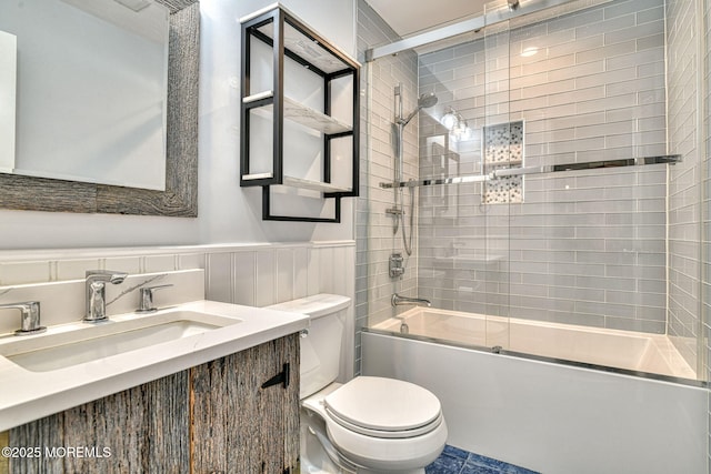 full bath featuring a wainscoted wall, vanity, toilet, and bath / shower combo with glass door