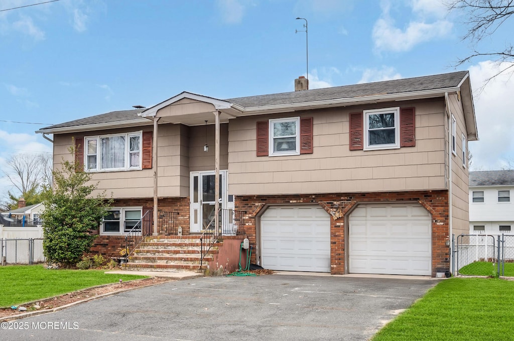 split foyer home featuring aphalt driveway, brick siding, an attached garage, and fence