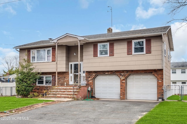 split foyer home featuring aphalt driveway, brick siding, an attached garage, and fence