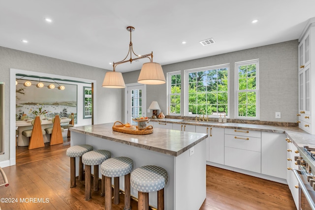 kitchen with wood finished floors, white cabinetry, a kitchen island, a sink, and high end stainless steel range oven