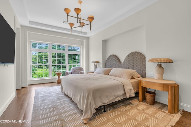 bedroom with wood finished floors, baseboards, visible vents, an inviting chandelier, and a tray ceiling