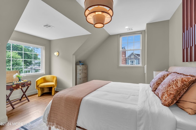 bedroom with lofted ceiling, wood finished floors, visible vents, and baseboards