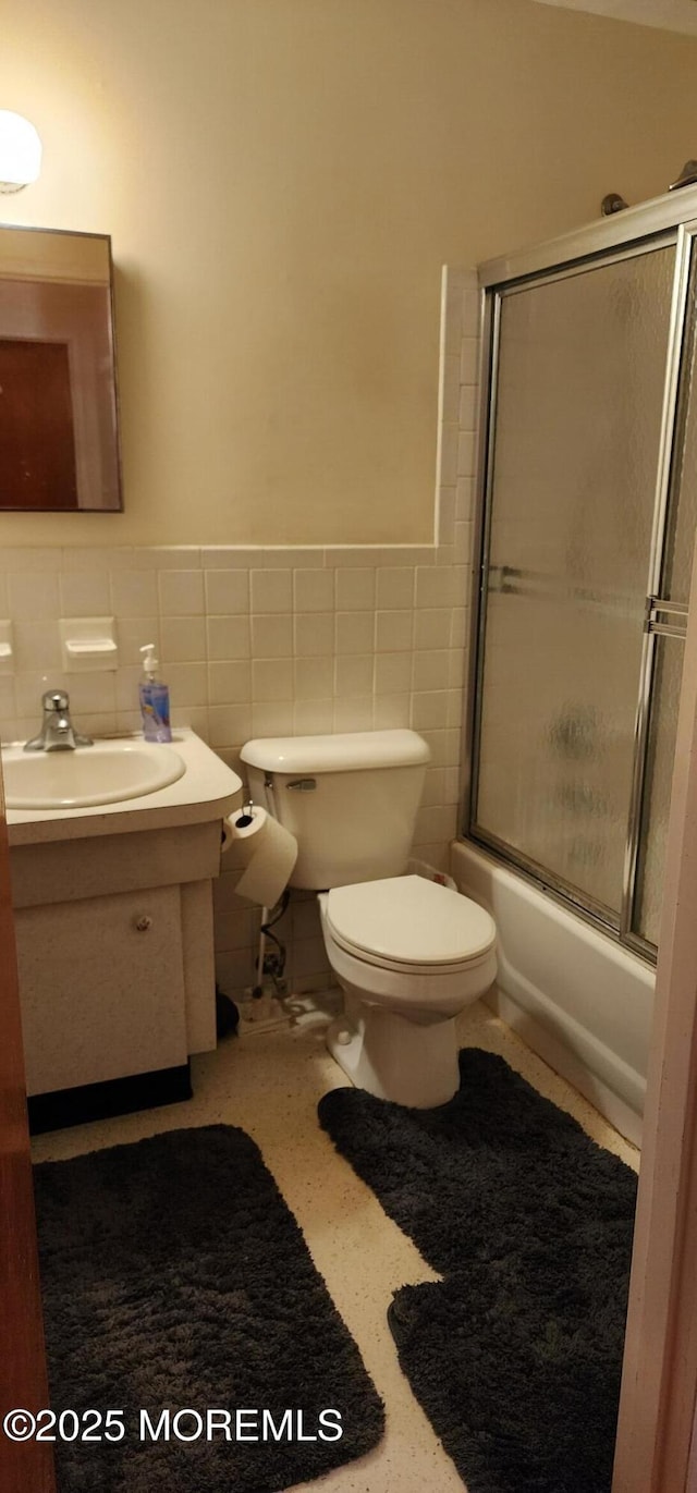 bathroom featuring a wainscoted wall, toilet, vanity, shower / bath combination with glass door, and tile walls