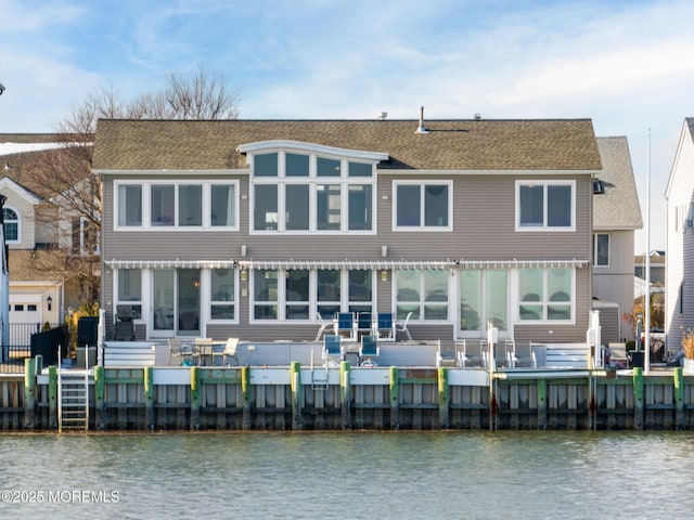 back of house with a shingled roof and a deck with water view