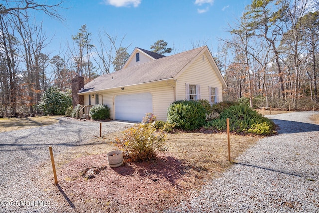 view of side of home with an attached garage, gravel driveway, a chimney, and a shingled roof