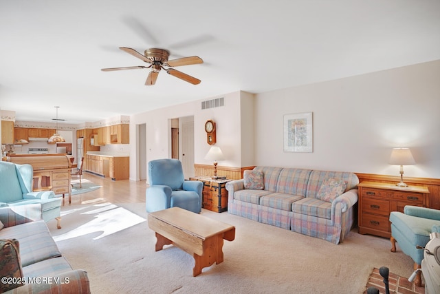 living area featuring visible vents, a wainscoted wall, light carpet, and ceiling fan