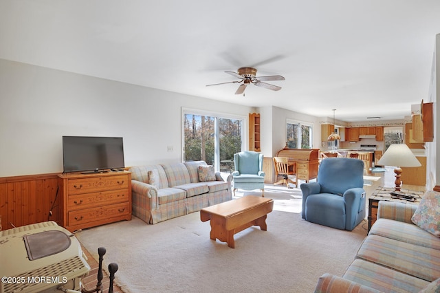 living area featuring wooden walls, a wainscoted wall, light colored carpet, and a ceiling fan