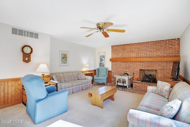 living room featuring visible vents, light colored carpet, a wood stove, and a ceiling fan